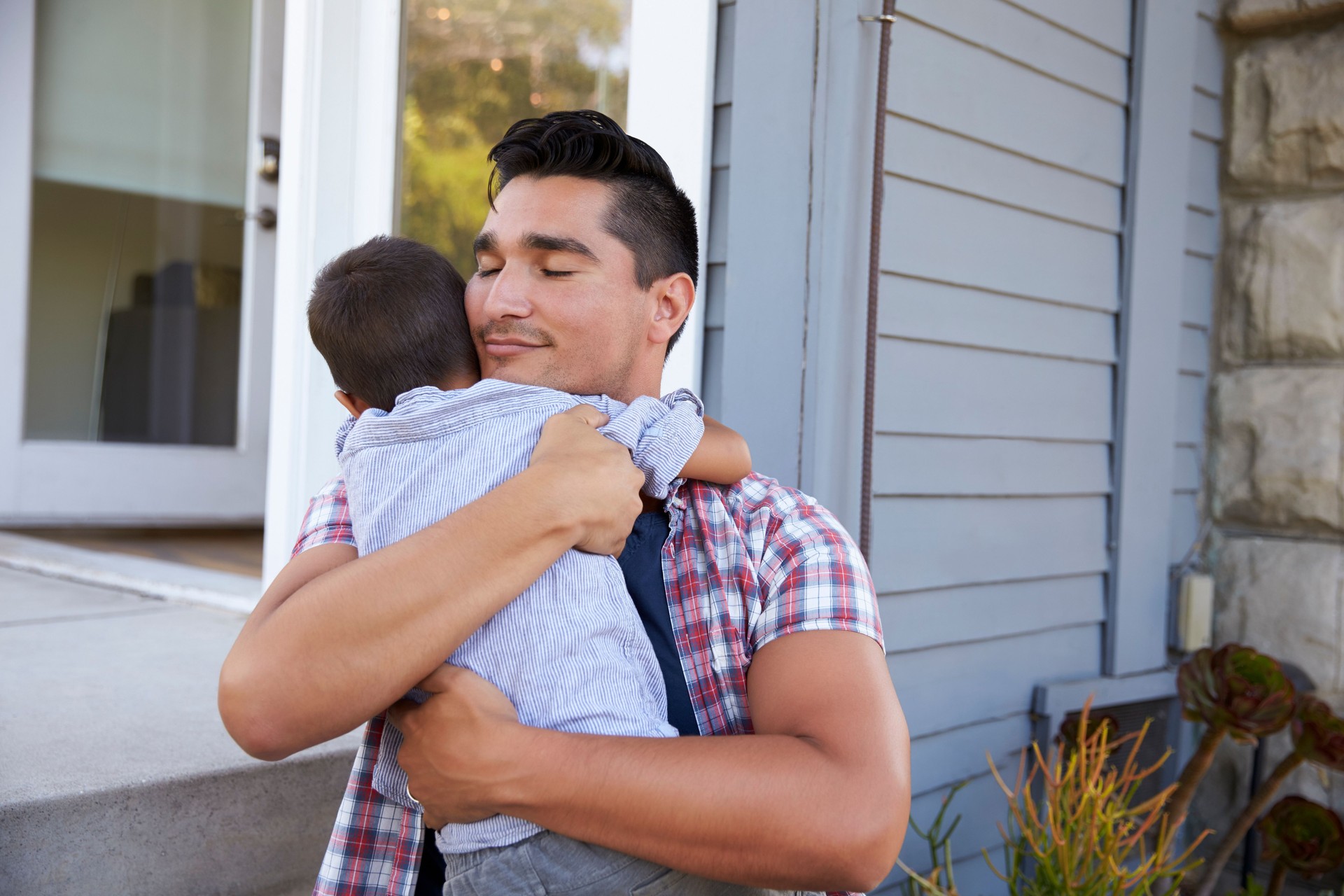 Father Hugging Son Sitting On Steps Outside Home